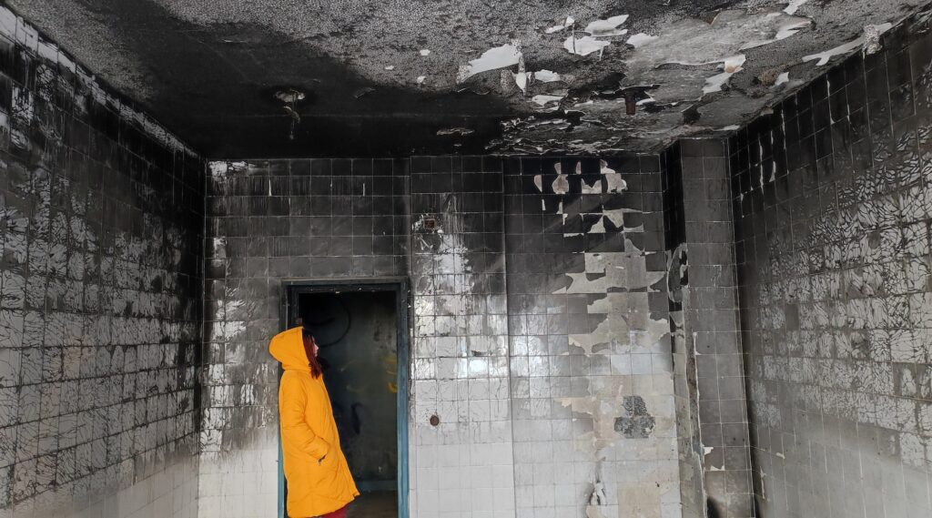 Young woman in yellow hoodie jacket on the door of a room after the fire